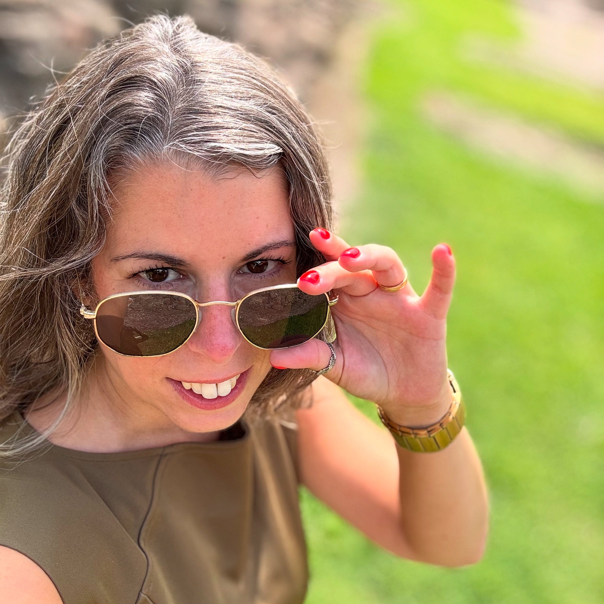 Su Dias, founder of P’tit Affair, wearing an olive green petite midi dress and sunglasses, smiling outdoors. Founder of a slow fashion brand for petite women