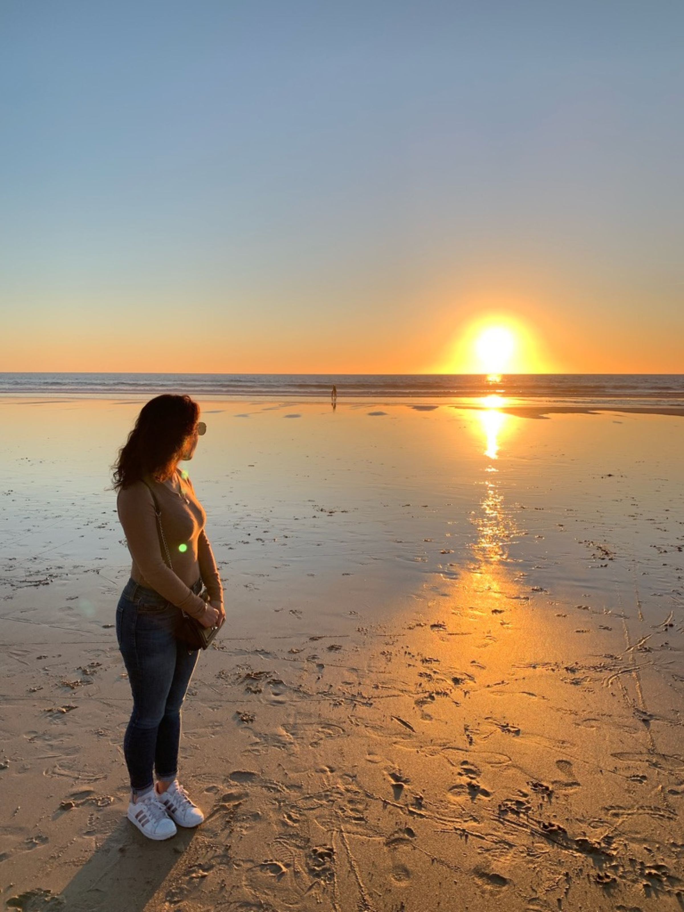 Woman standing on the beach at sunset in Portugal, reflecting the inspiration behind P’tit Affair’s timeless and soulful fashion