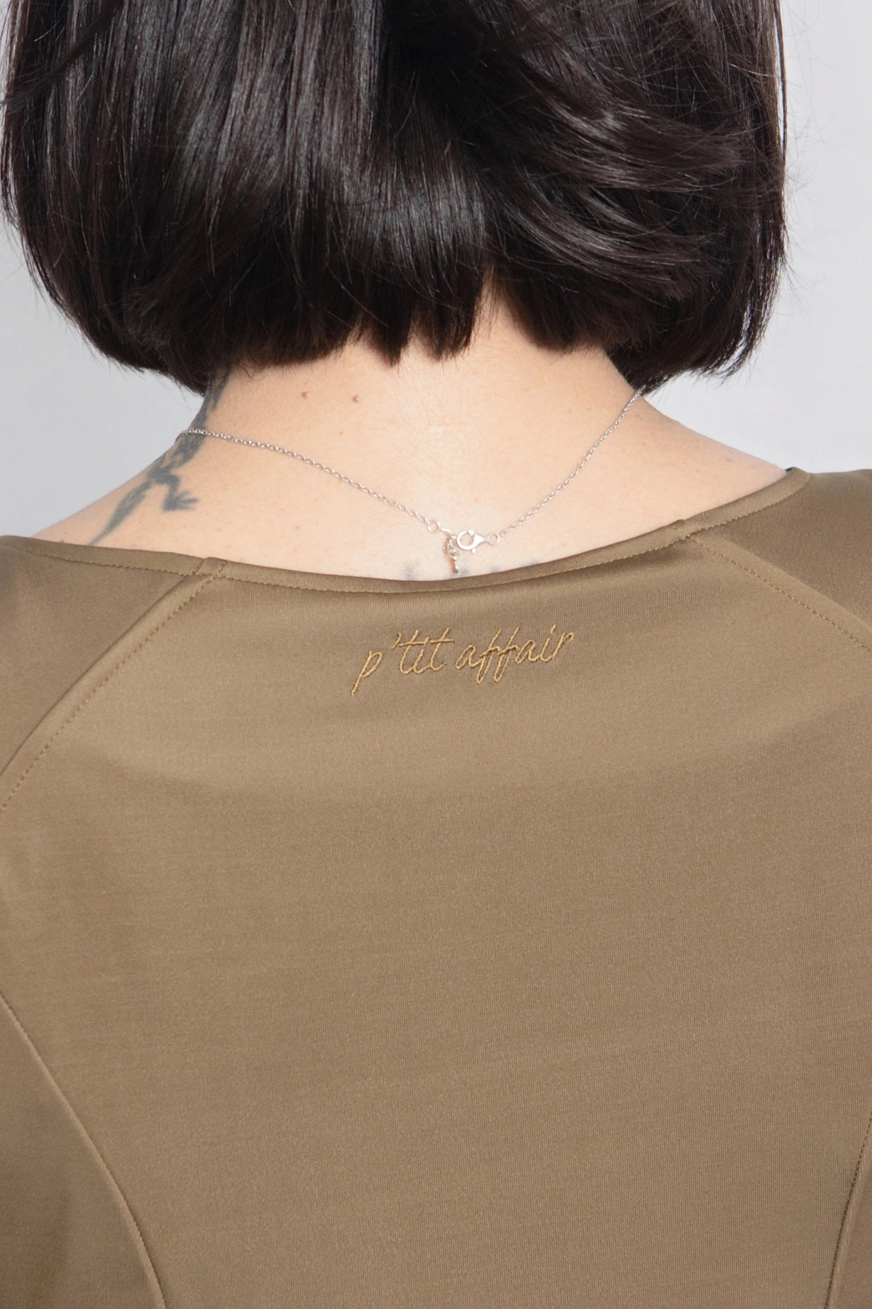 Close-up of P’tit Affair Eloise Midi Dress in olive green showing embroidered logo detail on the back neckline