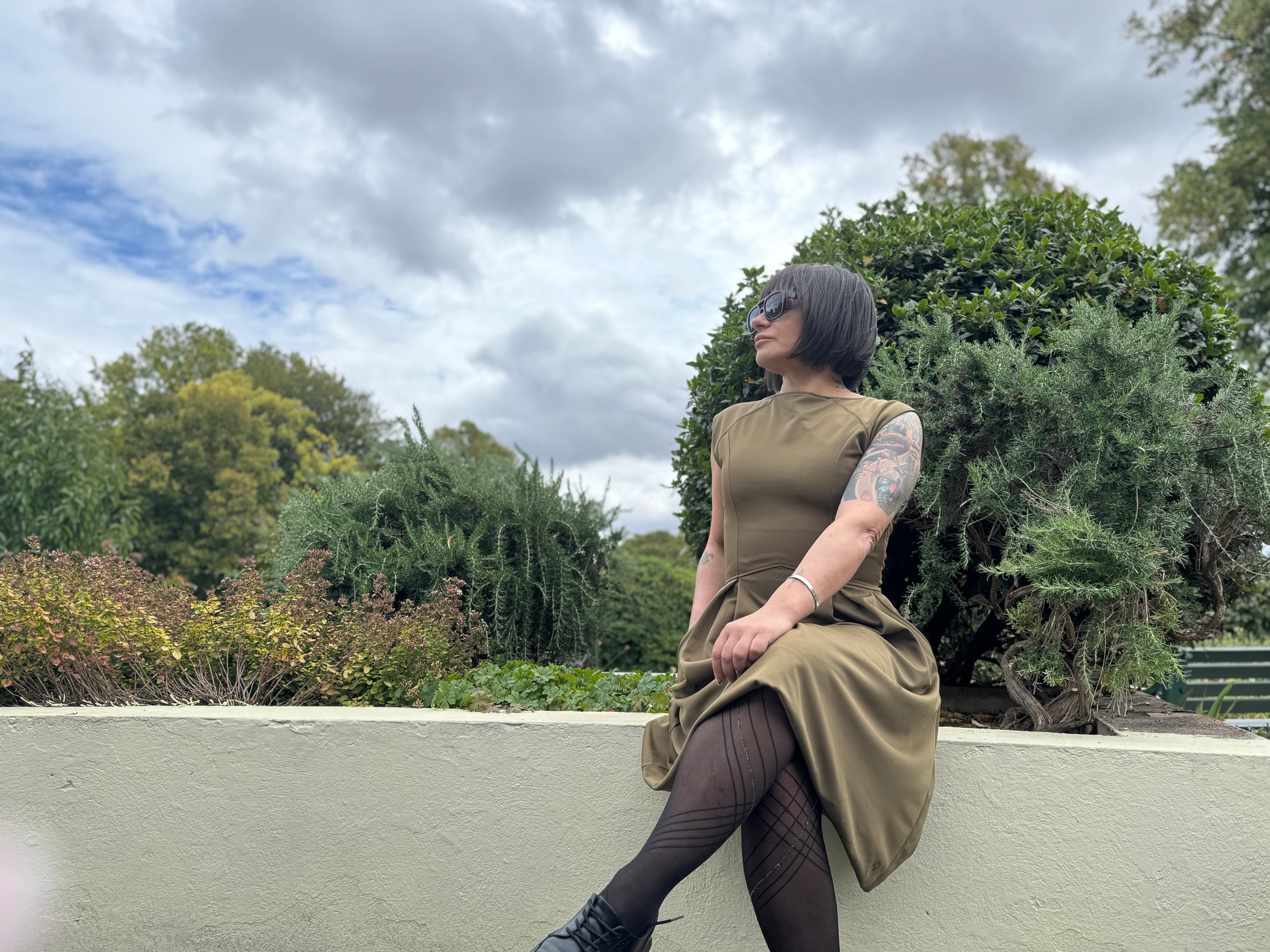 Petite woman wearing the P’tit Affair Eloise Midi Dress in Olive green, timeless fashion designed for women 5’3” and under, photographed outdoors in a park.