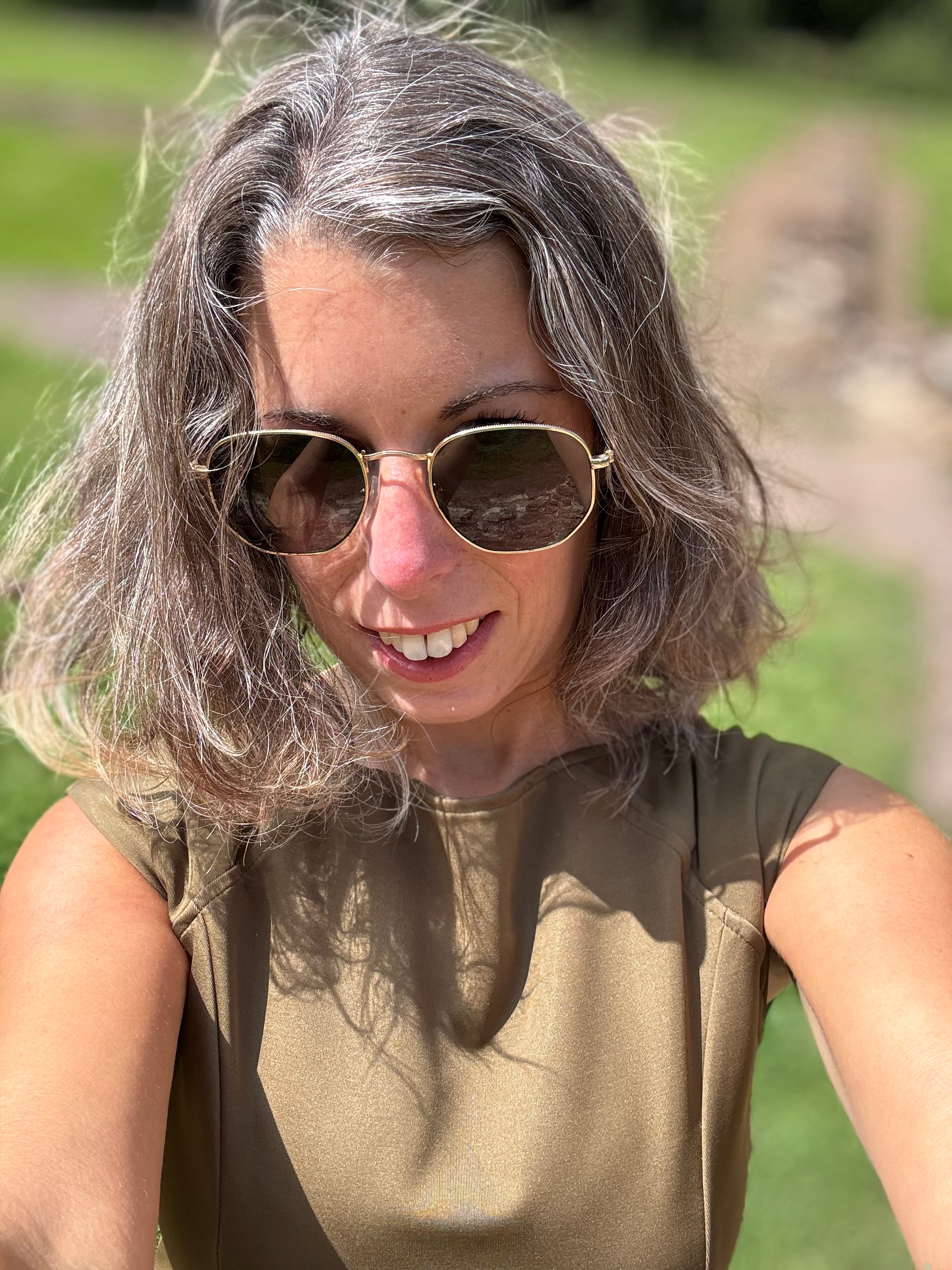 Close-up of petite woman wearing P’tit Affair Eloise Midi Dress in olive outdoors, styled with sunglasses