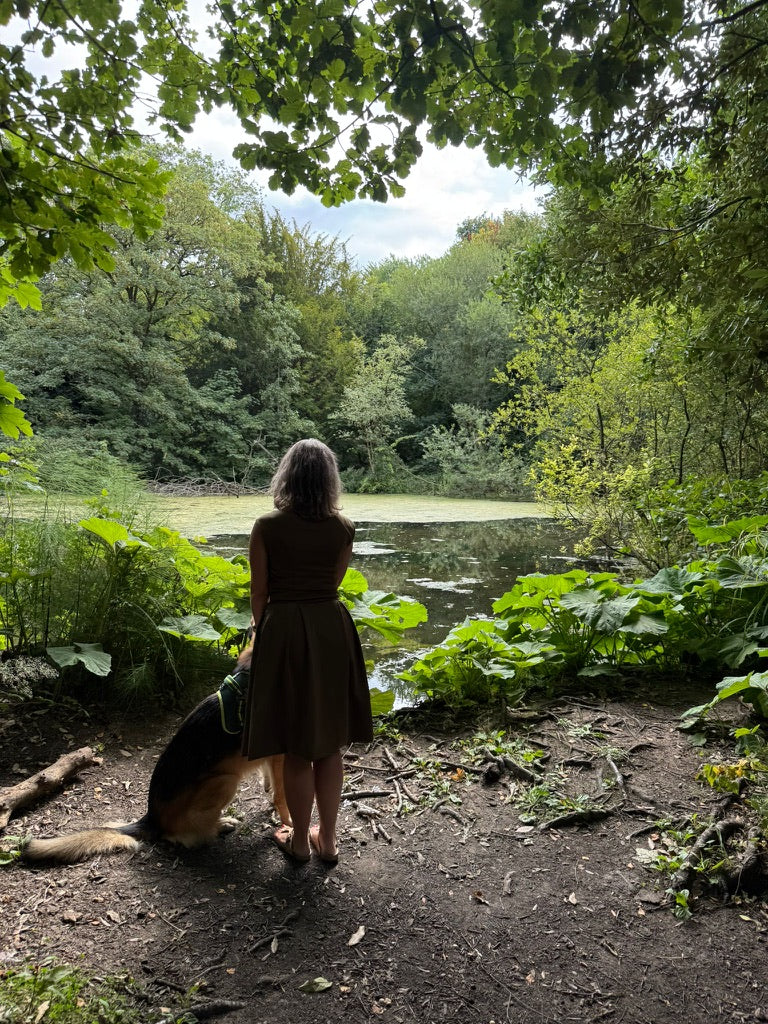 Woman in a petite midi dress with her dog by a lake, representing timeless fashion and empowering stories for petite women.
